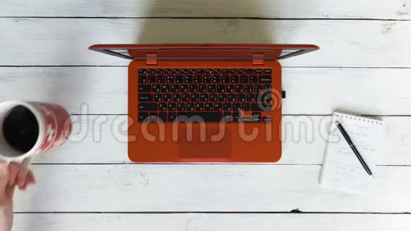 一个男人在一台红色的笔记本电脑上打字笔记本电脑放在一张白色的木桌上左边是一杯黑咖啡视频的预览图