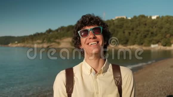 海滩上一个穿着时尚太阳镜的快乐卷发男人的肖像视频的预览图