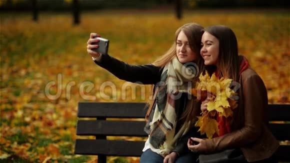 漂亮的女孩让自拍在长凳上的智能手机两位年轻女性喜欢户外活动和与自拍视频的预览图