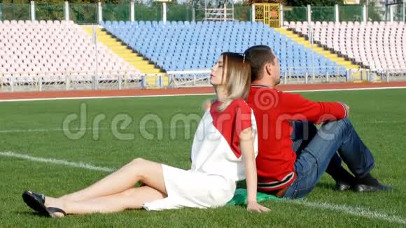 年轻人和漂亮的女孩坐在体育场足球场的中心视频的预览图