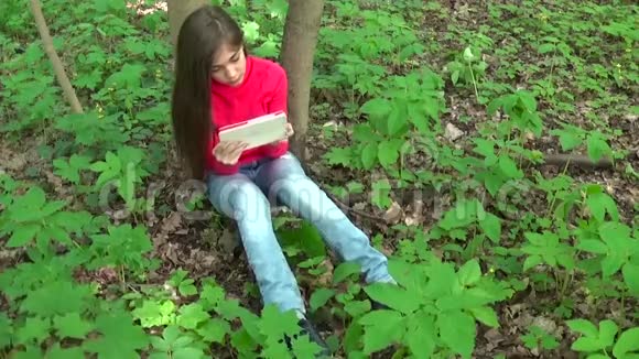 公园里坐在草地上的一个年轻漂亮的女孩手里拿着平板电脑静态摄像机的电影视频的预览图