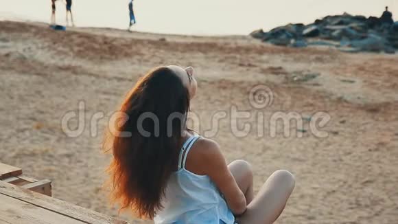 快乐的年轻女子坐在沙滩上看海视频的预览图