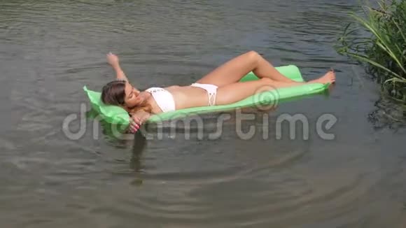 在床垫上漂浮在河中的白色比基尼的年轻晒黑的女人视频的预览图