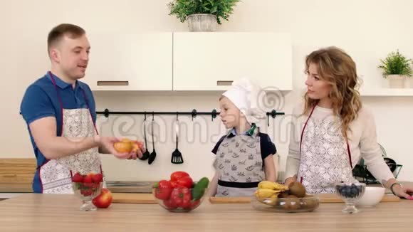 一家人正在厨房准备沙拉爸爸把苹果扔了起来儿子和他母亲在微笑视频的预览图