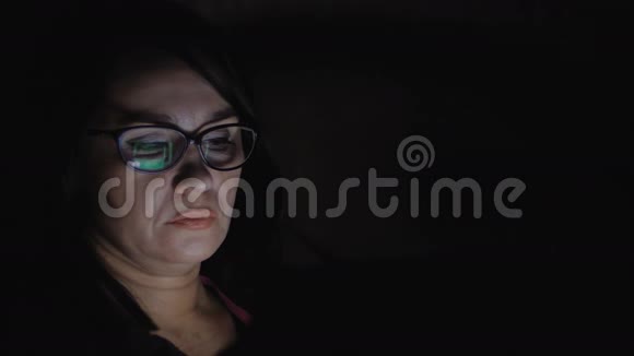 一个女人坐在黑暗的房间里的沙发上在平板电脑上工作视频的预览图