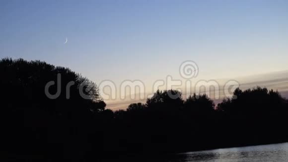 黄昏时分湖面上一轮新月背景中远处有一片森林和一架飞机的轮廓视频的预览图