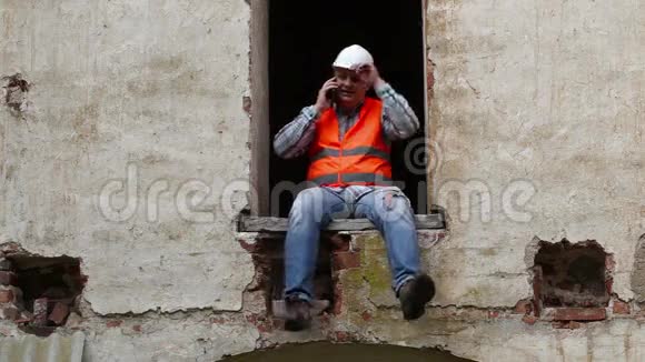 建筑工人坐在窗户上打电话视频的预览图