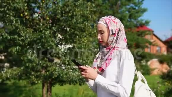 一位戴着头巾的年轻穆斯林妇女正在公园的智能手机上聊天视频的预览图