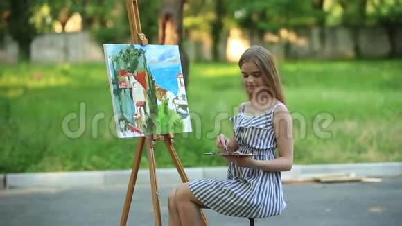 美丽的女孩艺术家坐在公园的凳子上拿着颜料调色板视频的预览图