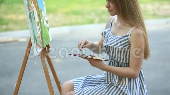 美丽的女孩艺术家坐在公园的凳子上拿着颜料调色板视频的预览图