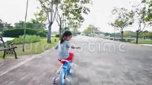 一个亚洲小女孩骑着自行车在公共公园里带着摄像机视频的预览图