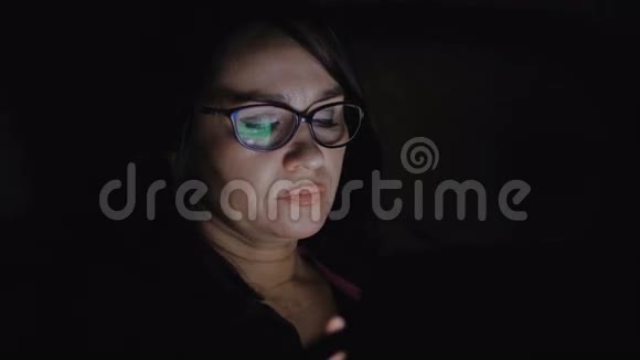 一个女人坐在黑暗的房间里的沙发上在平板电脑上工作视频的预览图