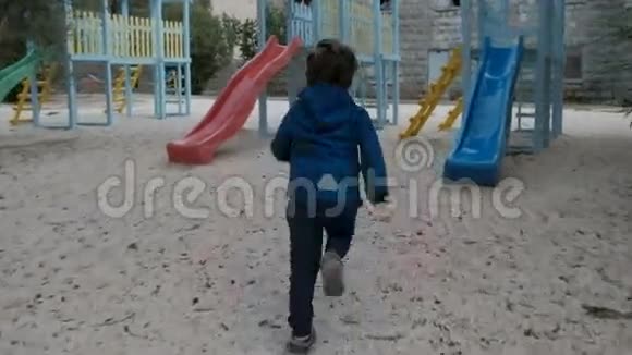 在凉爽的一天小男孩在操场上骑着塑料滑梯视频的预览图