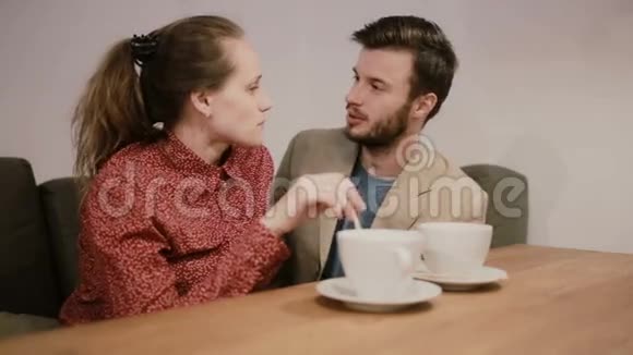 一对相爱的夫妇坐在桌子上的沙发上上面有空咖啡杯他们在说话微笑接吻视频的预览图