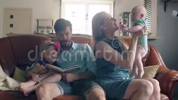 四口之家正坐在沙发上聊天妈妈抱着她可爱的微笑宝宝4k视频的预览图