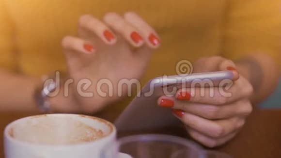 坐在咖啡桌旁的女人用她修剪过的纤细手指在手机上打字视频的预览图