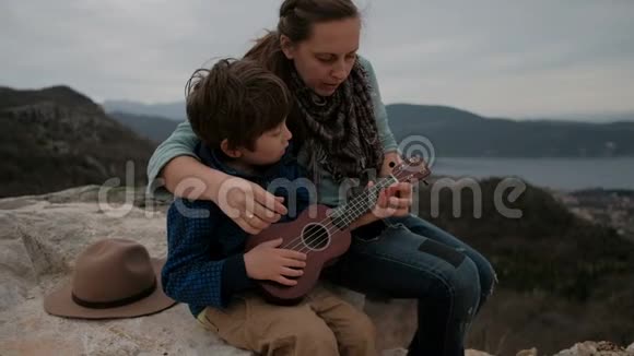 母亲教儿子在石头上坐在一起弹吉他视频的预览图