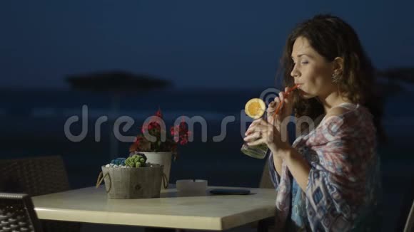 微笑的年轻女士在海边餐厅喝鸡尾酒写在笔记本上视频的预览图