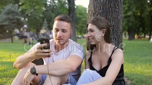 在树下的公园里听音乐的男人和女孩视频的预览图