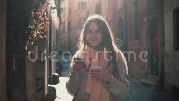 年轻微笑的女人早上在城市里散步用智能手机女孩浏览互联网和某人发短信视频的预览图