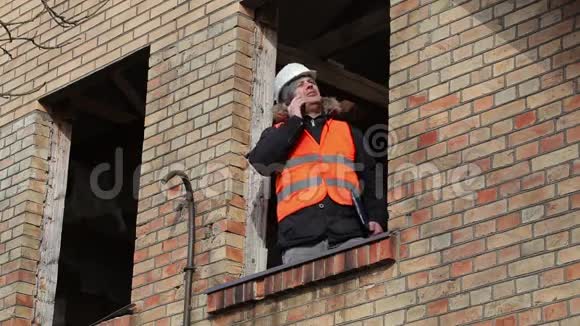 工地经理在大楼二楼窗户上用智能手机说话视频的预览图