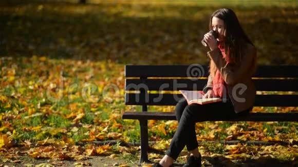 美丽的高加索女人在秋季公园的长凳上喝咖啡和看书户外放松的概念视频的预览图