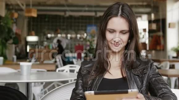 时尚的年轻女性使用平板电脑发送短信坐在现代咖啡馆的桌子上奇迹微笑4K视频的预览图