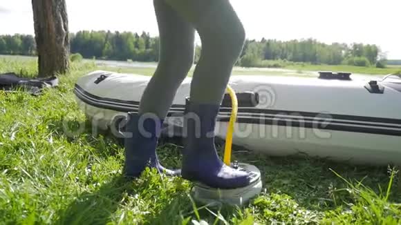 穿橡胶靴的妇女在青草上用抽水机给漂流船充气高清慢行视频的预览图