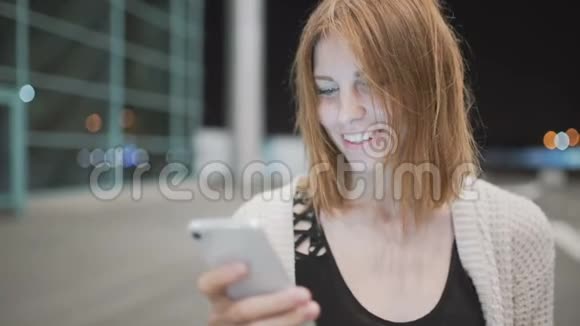 年轻漂亮的红发女人用她的手机写信息城市之夜的背景视频的预览图