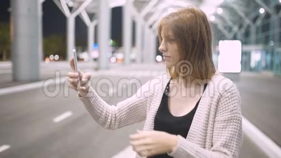 年轻漂亮的红发女人用她的手机写信息城市之夜的背景视频的预览图