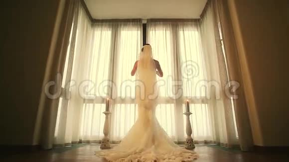 穿着婚纱的新娘的后侧来到窗口揭开白色的窗帘暖色调视频的预览图