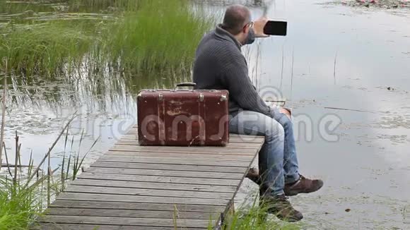 带着手提箱的人坐在湖边拍照视频的预览图