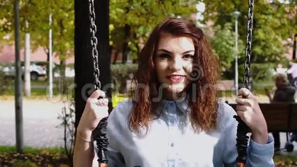 年轻红发女子在公园里荡秋千视频的预览图