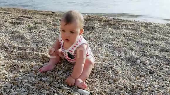 一个戴着白色帽子的孩子坐在海滩上的一块鹅卵石上视频的预览图