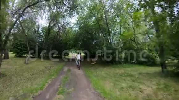 在公园里骑自行车在森林小径上骑自行车的女孩慢动作视频的预览图