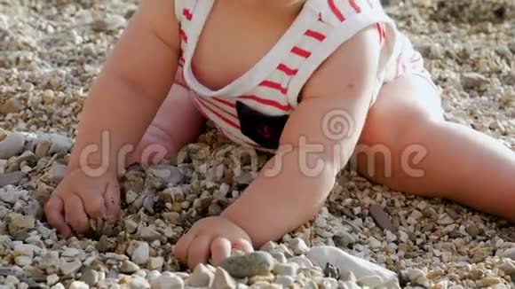 一个戴着白色帽子的孩子坐在海滩上的一块鹅卵石上视频的预览图