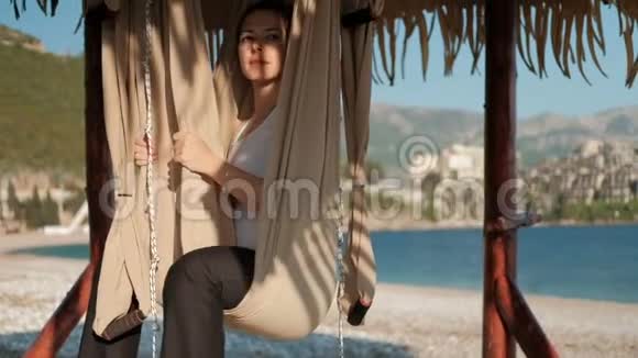 女人坐在阳光明媚的海滩上的吊床上看着远处视频的预览图