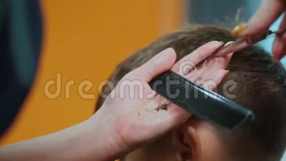 在美发沙龙剪小男孩头发的理发师的双手合拢视频的预览图