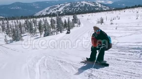 在一个阳光明媚的冬天在雪山上骑着一条绳子穿着颜色鲜艳的夹克和太阳镜的快乐男子滑雪板视频的预览图