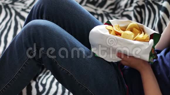 一个十几岁的男孩在家里用手在沙发上吃薯片视频的预览图