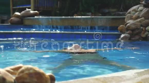 布鲁内特微笑着在阳光明媚的日子里女人在游泳池里慢动作地享受着水在美丽的阳光下度假视频的预览图