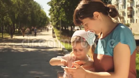 小女孩和她的妈妈坐在公园的长椅上享受电话视频的预览图