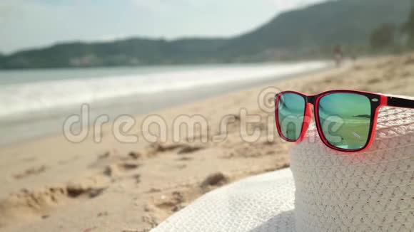 太阳镜和白色宽边躺在沙子上戴着墨镜反射着大海海浪和天空视频的预览图