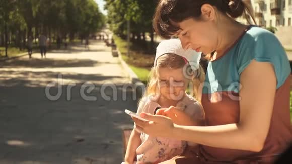 小女孩和她的妈妈坐在公园的长椅上享受电话视频的预览图