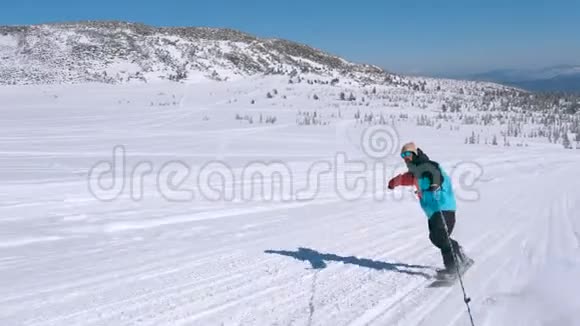 在一个阳光明媚的冬天在雪山上骑着一条绳子穿着颜色鲜艳的夹克和太阳镜的快乐男子滑雪板视频的预览图