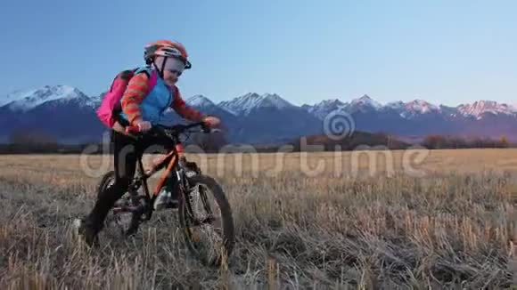 一个高加索儿童在麦田里骑自行车小女孩骑着黑色橙色自行车在美丽的雪背景下视频的预览图