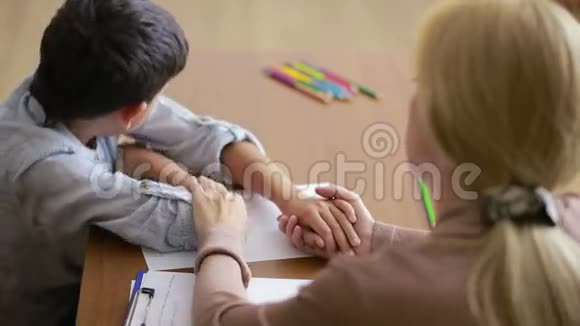 男孩在与年轻的心理学家交谈时沉默地坐着握着手视频的预览图