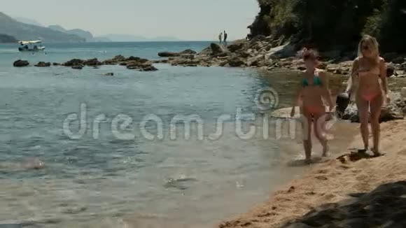 两个穿着比基尼的女人在山边的公共海滩上散步视频的预览图