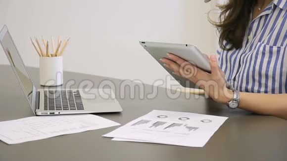 年轻的女人在工作在家里坐在桌子上时使用平板电脑视频的预览图