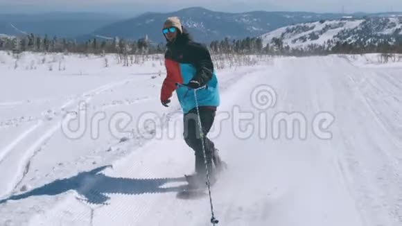 在一个阳光明媚的冬天在雪山上骑着一条绳子穿着颜色鲜艳的夹克和太阳镜的快乐男子滑雪板视频的预览图